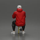 man in hoodie and cap sitting and putting his hand on the skateboard - Only-Games