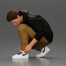 Man in hoodie crouching down tying shoelaces focused in casual outfit - Only-Games