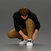 Man in hoodie crouching down tying shoelaces focused in casual outfit - Only-Games