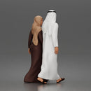 Walking man wearing thobe holding hands with woman wearing abaya