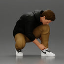 Man in hoodie crouching down tying shoelaces focused in casual outfit - Only-Games