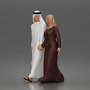 Walking man wearing thobe holding hands with woman wearing abaya