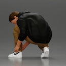 Man in hoodie crouching down tying shoelaces focused in casual outfit - Only-Games