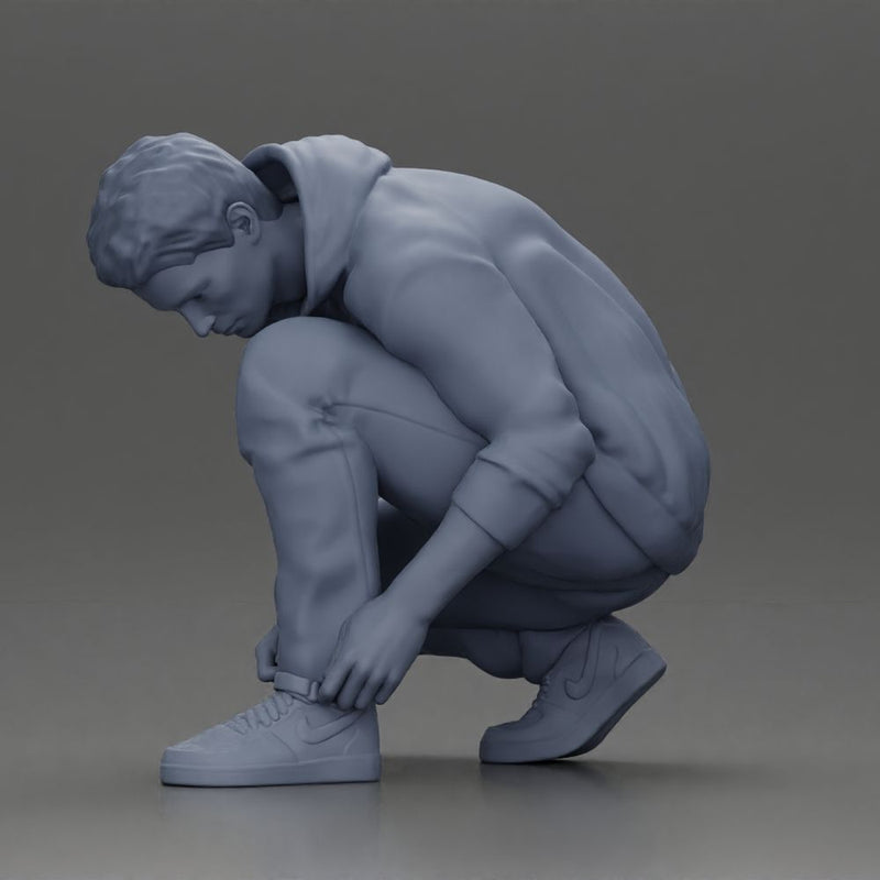 Man in hoodie crouching down tying shoelaces focused in casual outfit - Only-Games