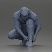 Man in hoodie crouching down tying shoelaces focused in casual outfit - Only-Games