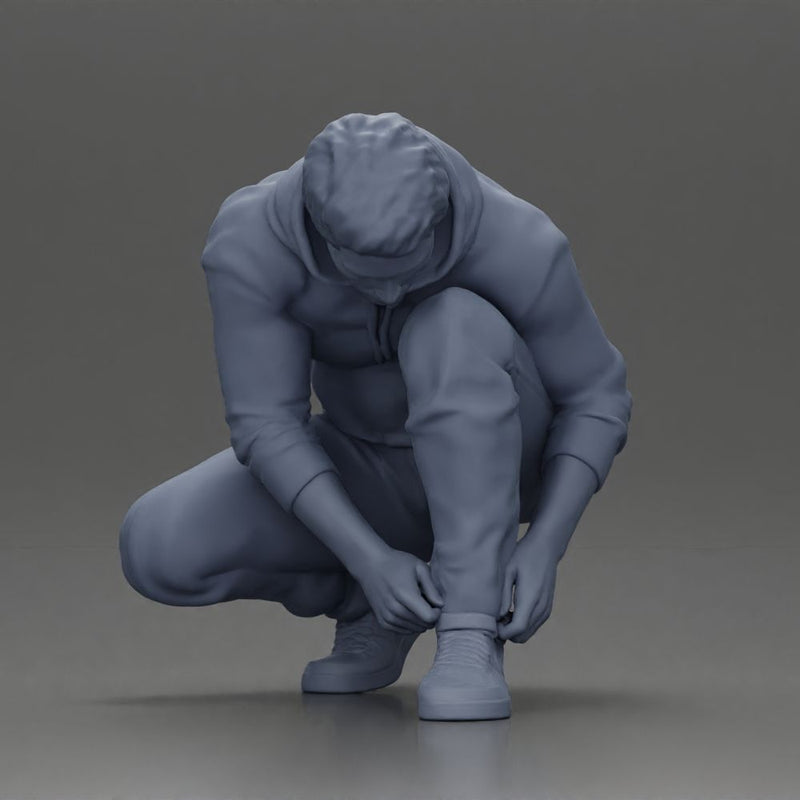 Man in hoodie crouching down tying shoelaces focused in casual outfit - Only-Games
