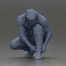 Man in hoodie crouching down tying shoelaces focused in casual outfit - Only-Games