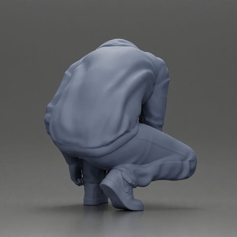 Man in hoodie crouching down tying shoelaces focused in casual outfit - Only-Games
