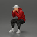 man in hoodie and cap sitting and putting his hand on the skateboard - Only-Games