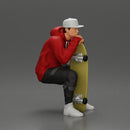 man in hoodie and cap sitting and putting his hand on the skateboard - Only-Games