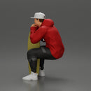 man in hoodie and cap sitting and putting his hand on the skateboard - Only-Games