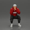 man in hoodie and cap sitting and putting his hand on the skateboard - Only-Games