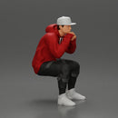 man in hoodie and cap sitting and putting his hand on the skateboard - Only-Games