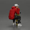 man in hoodie and cap sitting and putting his hand on the skateboard - Only-Games